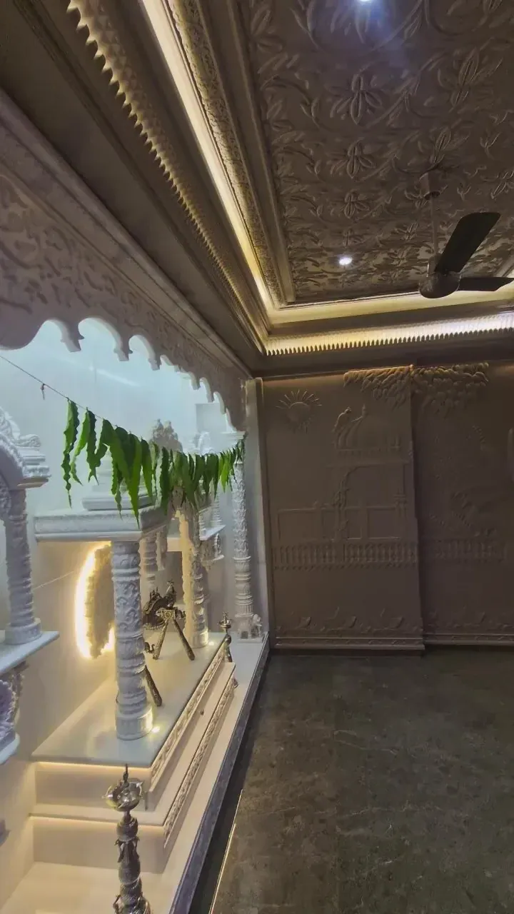 Carved white marble temple inside a pooja room with scalloped arch, fresh mango leaf toran and brass lamp
